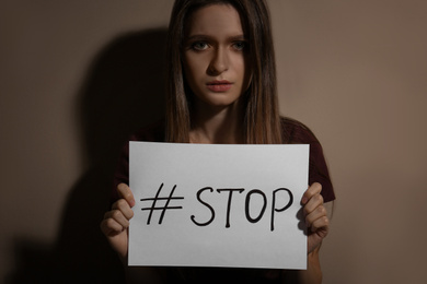 Photo of Abused young woman with hashtag STOP near beige wall. Domestic violence concept