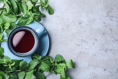 Photo of Cup with hot aromatic mint tea and fresh leaves on grey table, flat lay. Space for text