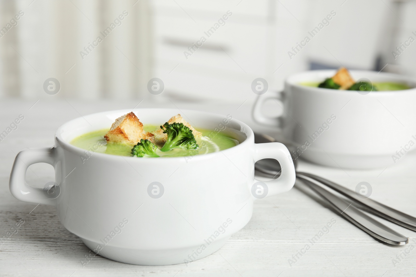 Photo of Delicious broccoli cream soup with croutons served on white wooden table indoors