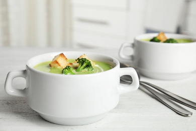 Delicious broccoli cream soup with croutons served on white wooden table indoors