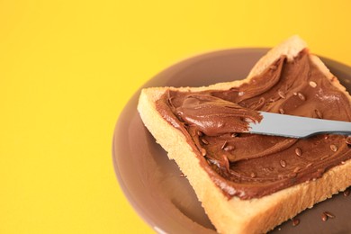 Photo of Spreading chocolate paste onto bread on yellow background, closeup. Space for text