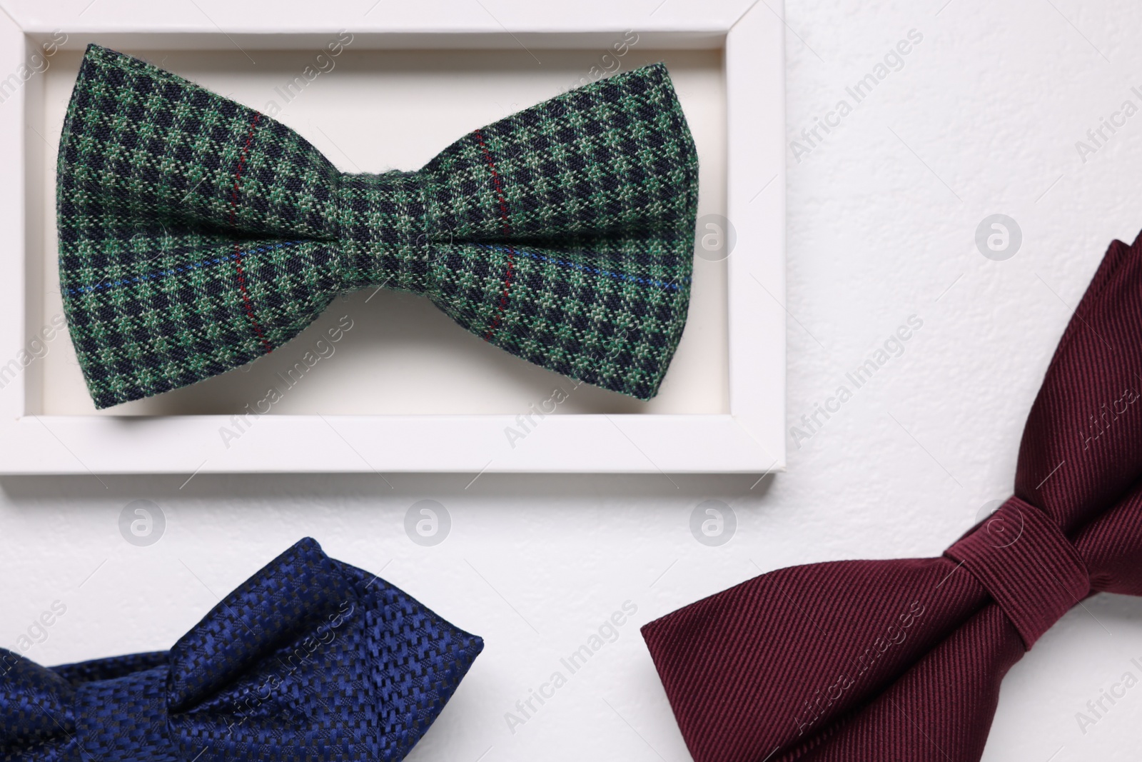 Photo of Stylish color bow ties on white textured background, flat lay