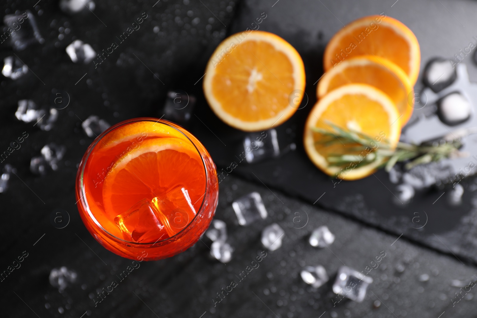 Photo of Glass of tasty Aperol spritz cocktail with orange slices and ice cubes on dark gray table, flat lay
