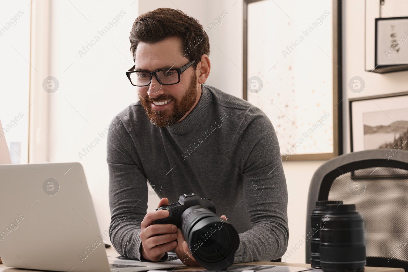 Photo of Professional photographer holding digital camera near table with laptop indoors