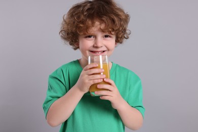 Photo of Cute little boy with glass of fresh juice on light gray background