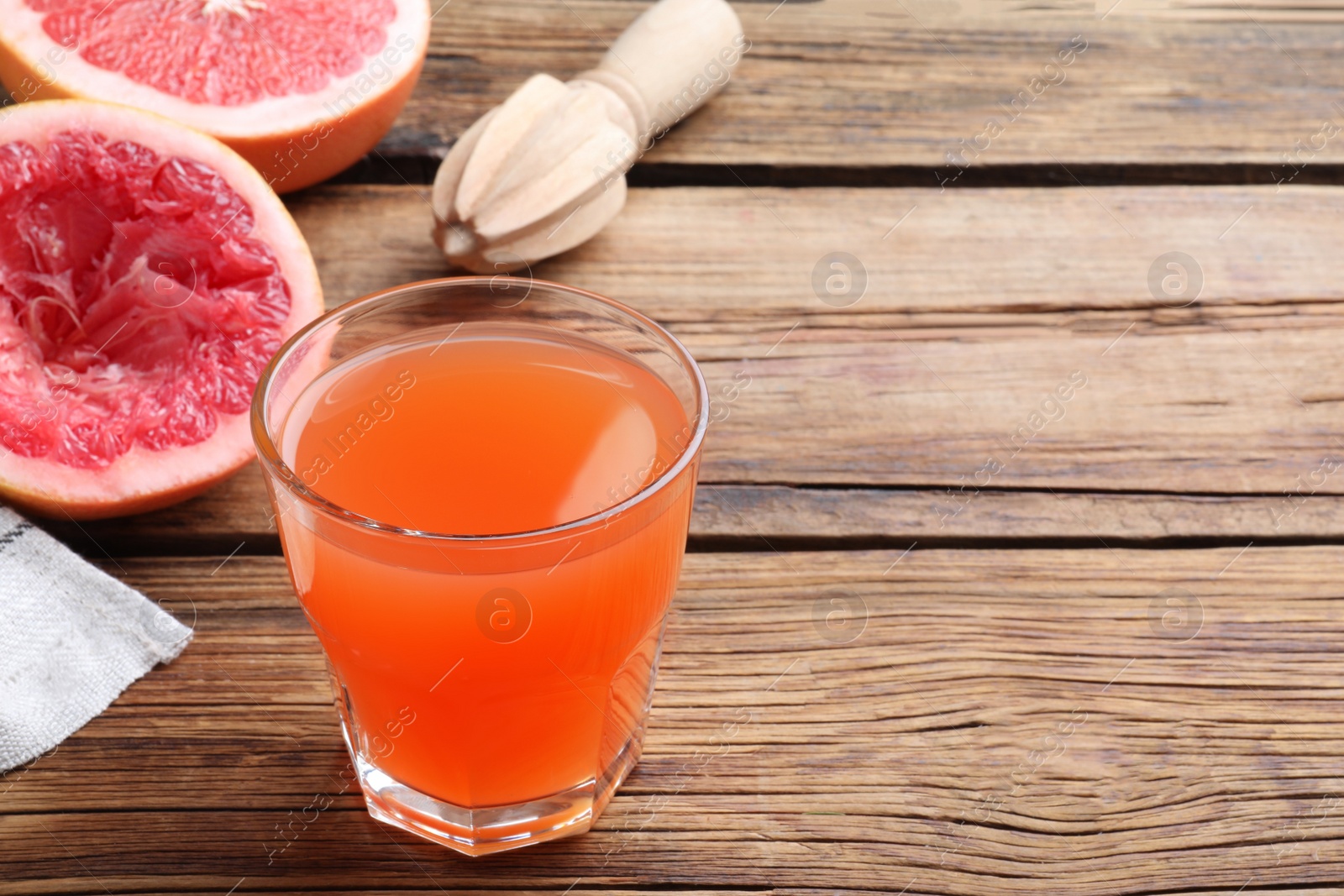 Photo of Tasty freshly made grapefruit juice on wooden table. Space for text