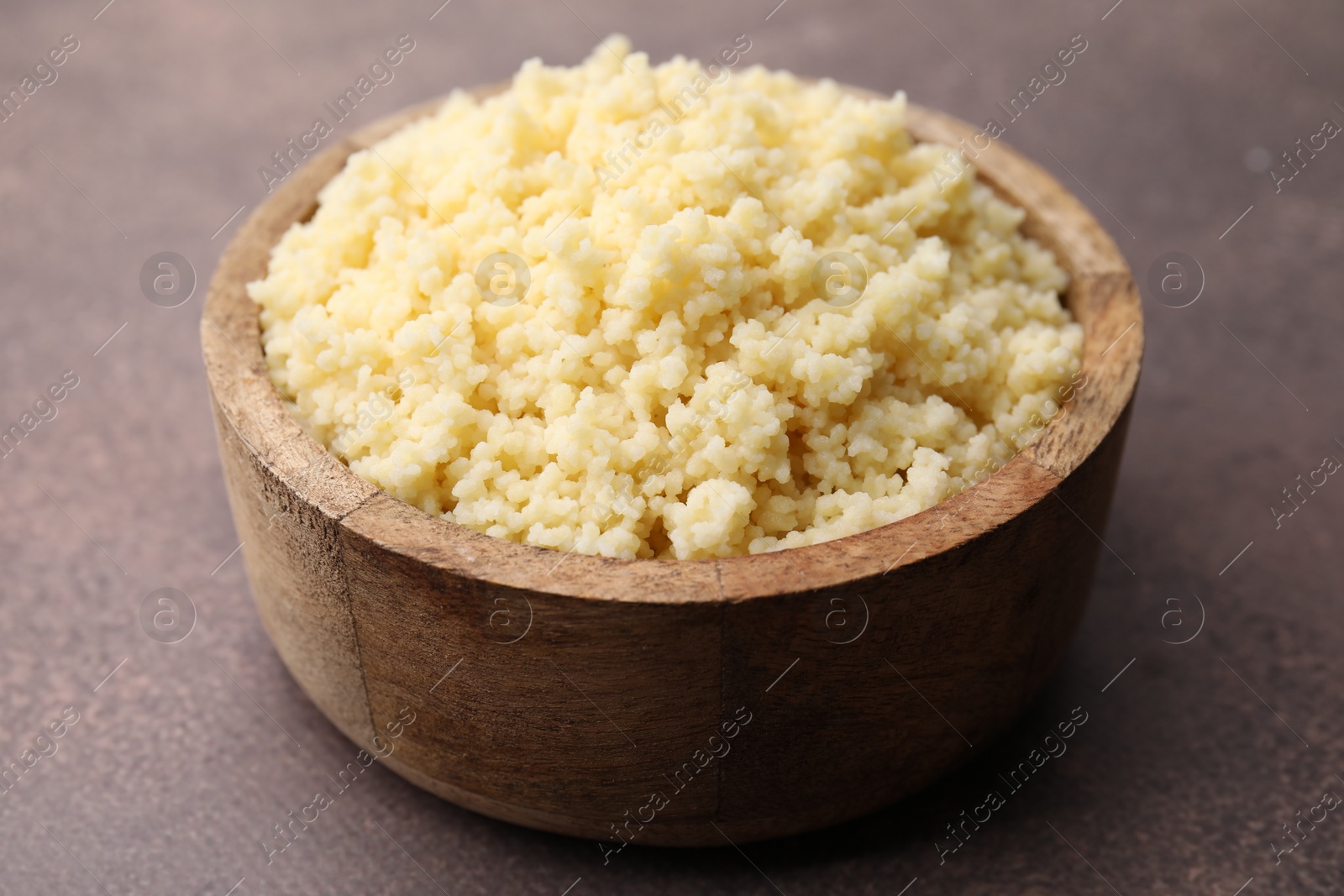 Photo of Tasty couscous in bowl on brown table, closeup