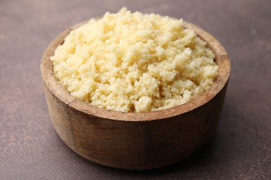 Photo of Tasty couscous in bowl on brown table, closeup