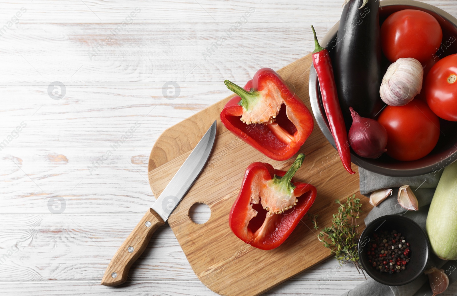 Photo of Cooking delicious ratatouille. Fresh ripe vegetables, knife and bowl on white wooden table, flat lay. Space for text