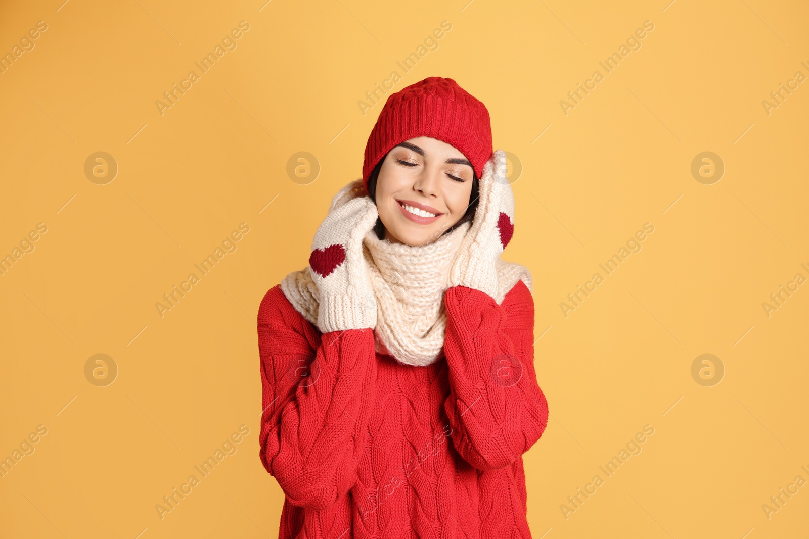 Photo of Young woman wearing warm sweater, scarf, mittens and hat on yellow background. Winter season