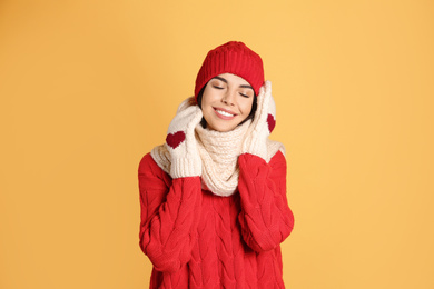 Photo of Young woman wearing warm sweater, scarf, mittens and hat on yellow background. Winter season