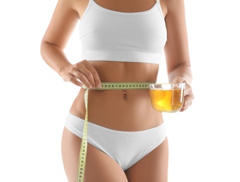 Photo of Young woman with measuring tape holding cup of diet tea on white background, closeup