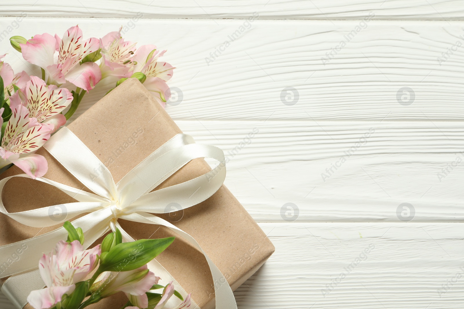 Photo of Happy Mother's Day. Beautiful flowers and gift box on white wooden table, flat lay. Space for text