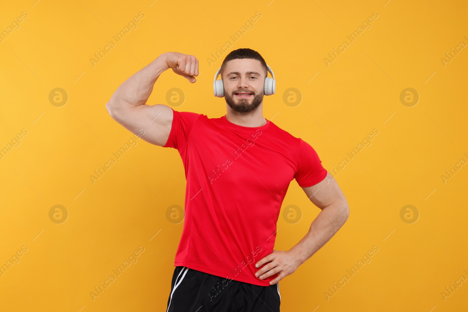 Photo of Handsome man with headphones showing muscles on yellow background