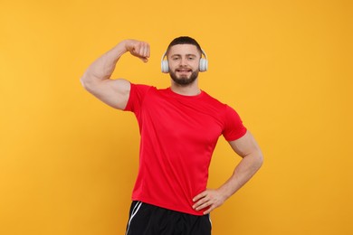 Photo of Handsome man with headphones showing muscles on yellow background
