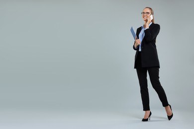 Photo of Happy young secretary with clipboard talking on smartphone against grey background, space for text