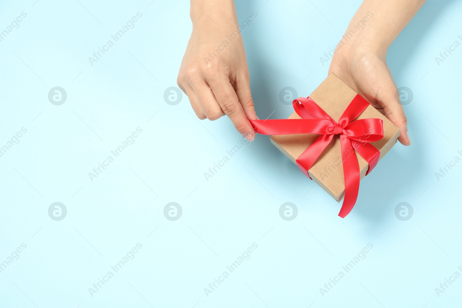 Photo of Woman holding gift box on light blue background, top view. Space for text