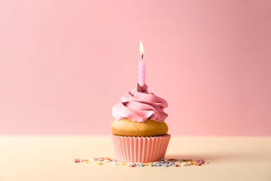 Delicious birthday cupcake with candle on color background