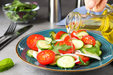 Photo of Woman adding cooking oil to delicious salad on grey table, closeup