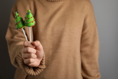 Photo of Woman holding delicious Christmas themed cake pops on grey background, closeup