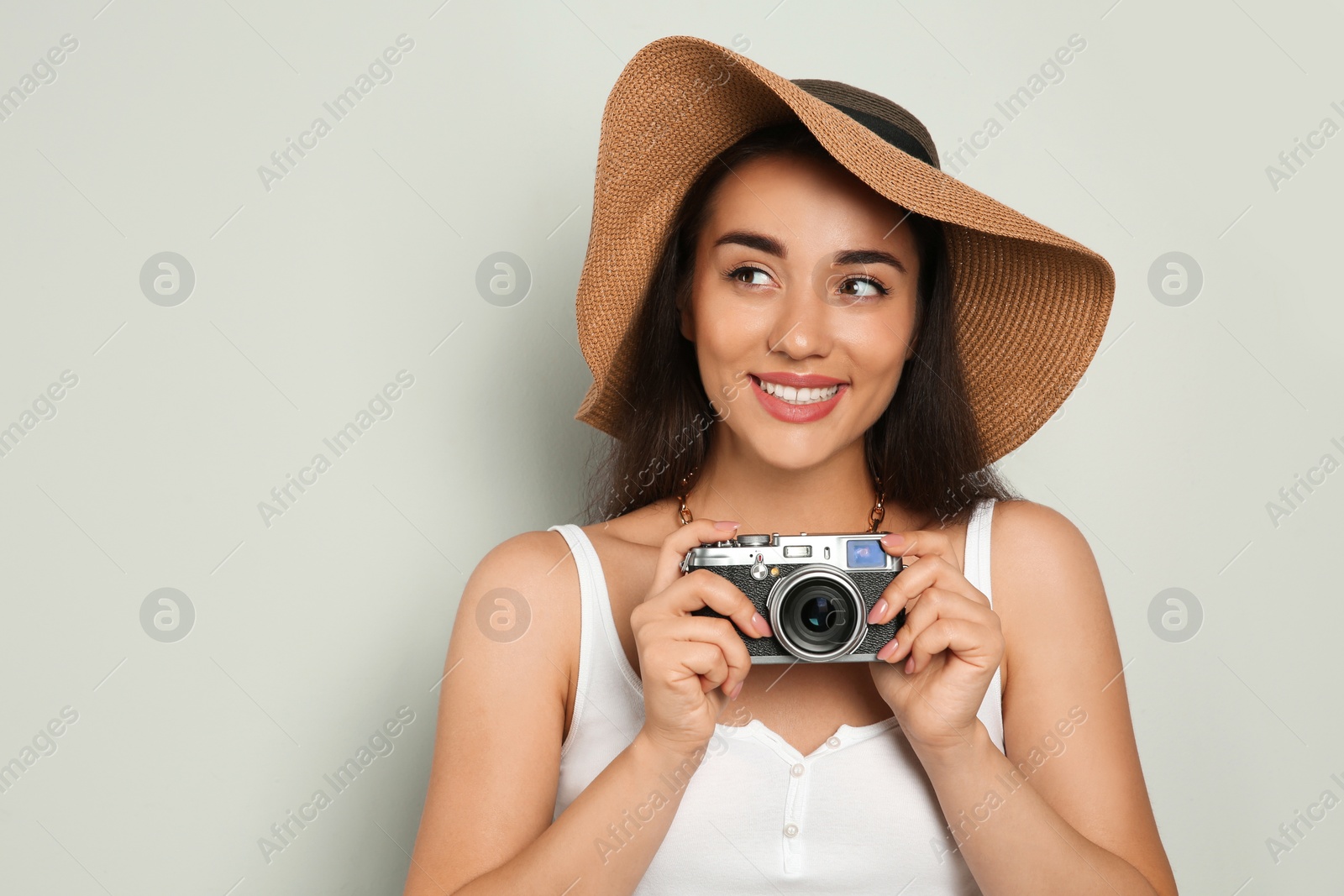 Photo of Beautiful young woman with straw hat and camera on light grey background, space for text. Stylish headdress