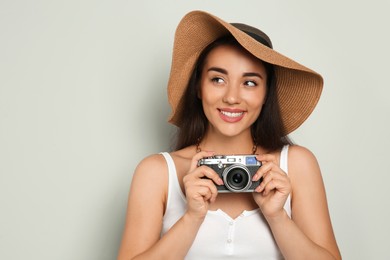 Photo of Beautiful young woman with straw hat and camera on light grey background, space for text. Stylish headdress