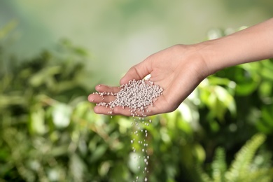 Woman pouring fertilizer on blurred background, closeup with space for text. Gardening time