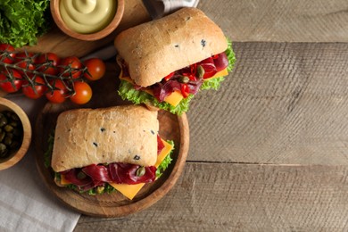 Photo of Delicious sandwiches with bresaola, cheese and lettuce served on wooden table, flat lay. Space for text