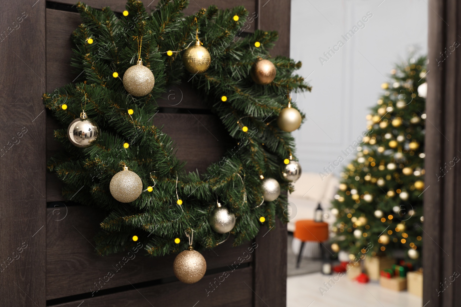 Photo of Christmas wreath with golden and silver baubles hanging on wooden door indoors