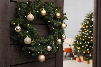 Christmas wreath with golden and silver baubles hanging on wooden door indoors