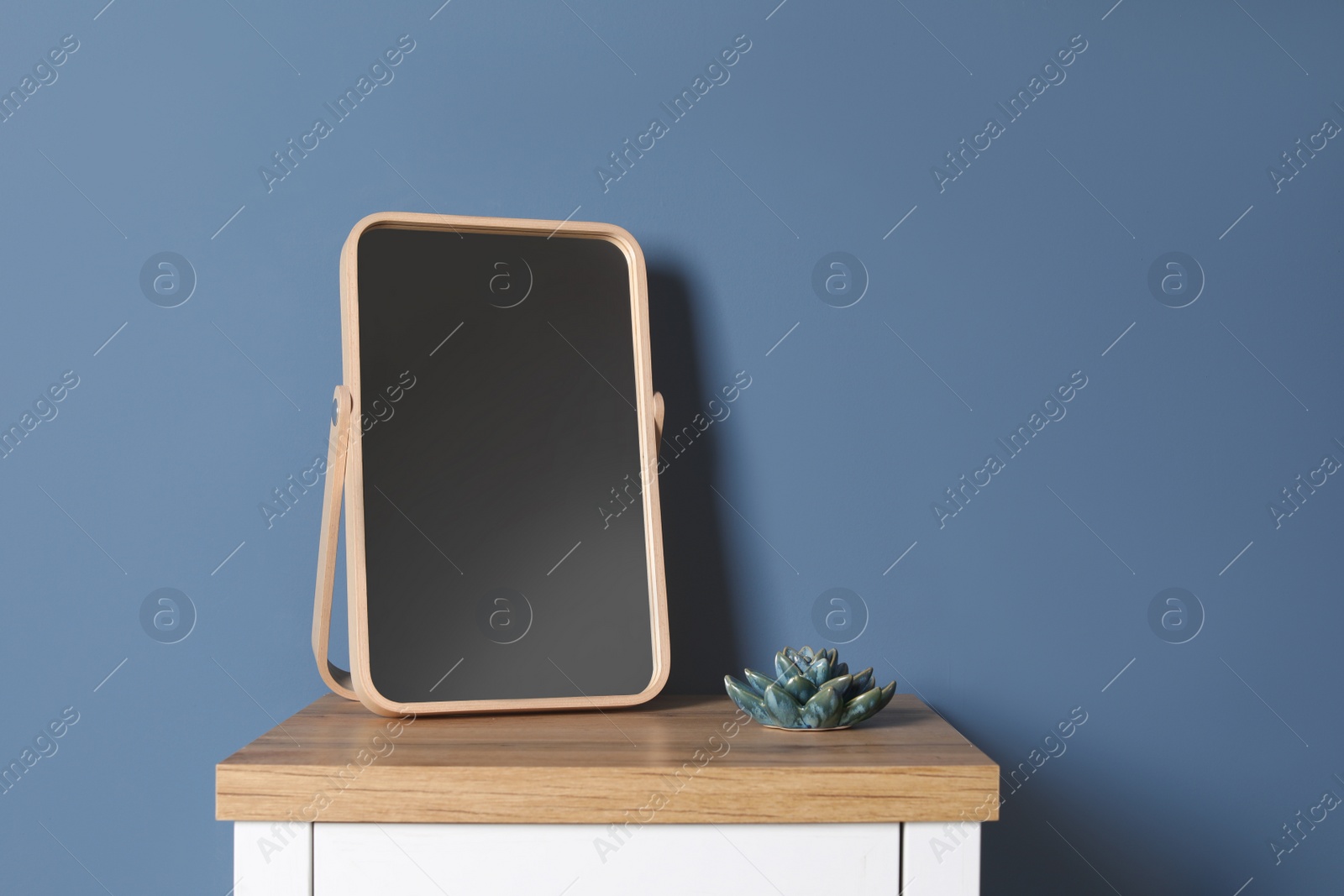 Photo of Modern mirror on table near color wall