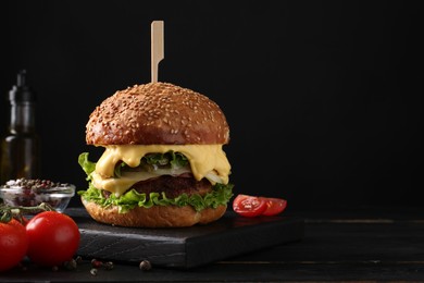 Photo of Tasty vegetarian burger, tomatoes and spices on black wooden table. Space for text