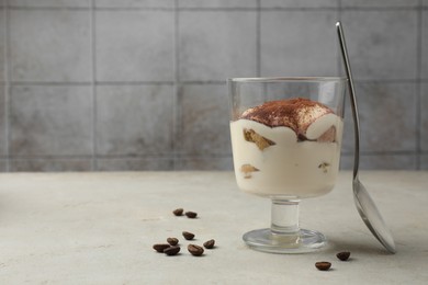 Photo of Delicious tiramisu in glass, spoon and scattered coffee beans on light table. Space for text