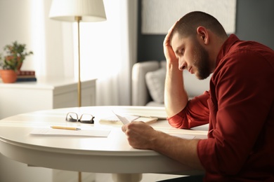 Photo of Man reading paper letter at white table in room