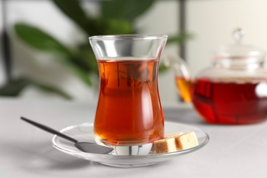 Photo of Traditional Turkish tea in glass and sugar cubes on white table, closeup