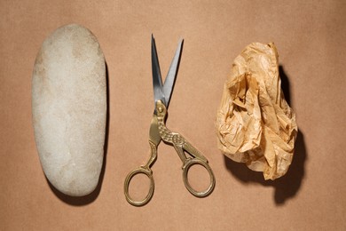 Photo of Rock, crumpled paper and scissors on light brown background, flat lay