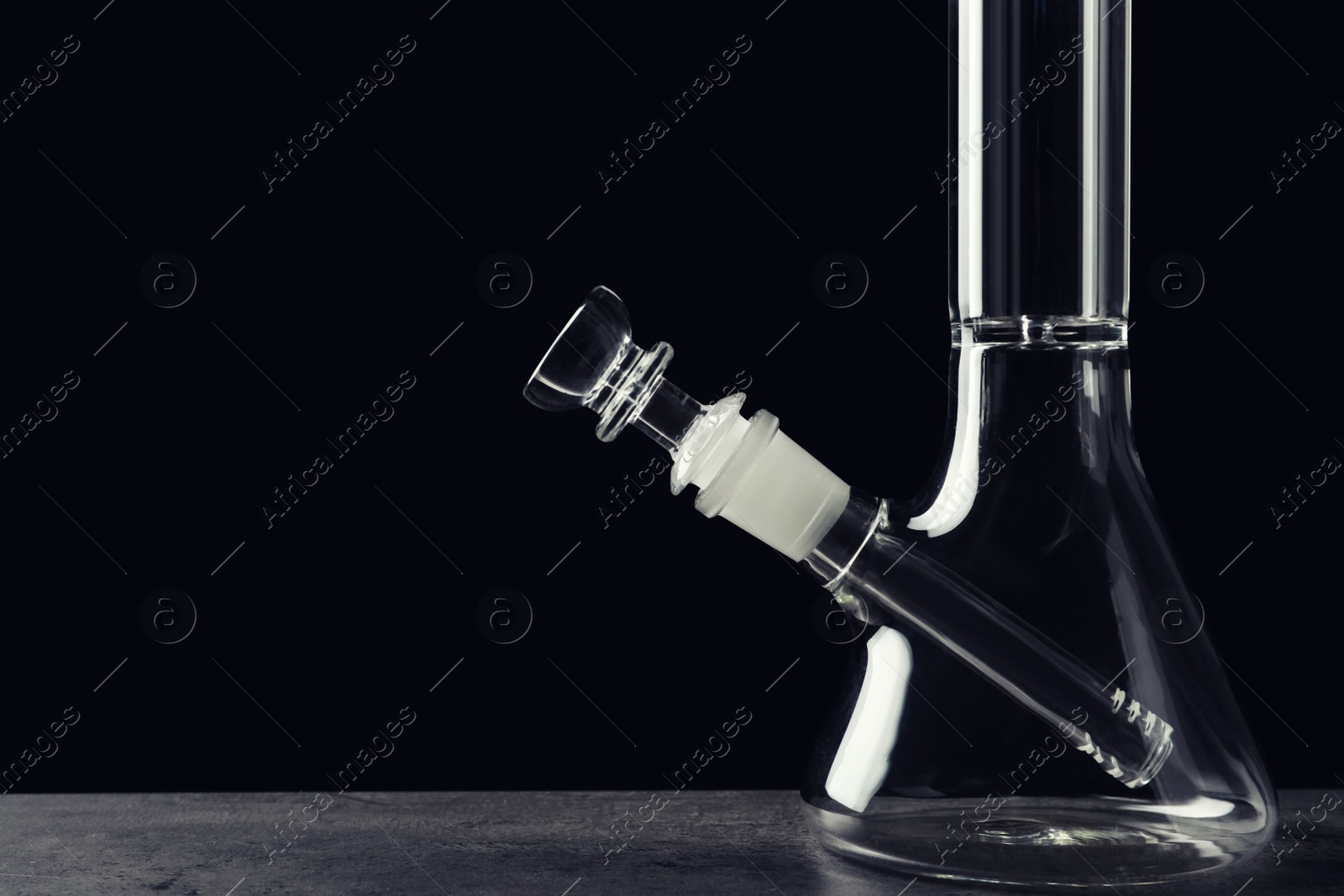 Photo of Glass bong on grey table against black background, space for text. Smoking device