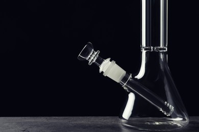 Glass bong on grey table against black background, space for text. Smoking device