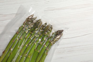 Photo of Asparagus in vacuum pack on white wooden table. Space for text