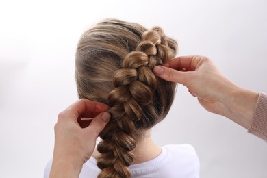Professional stylist braiding girl's hair on white background, closeup