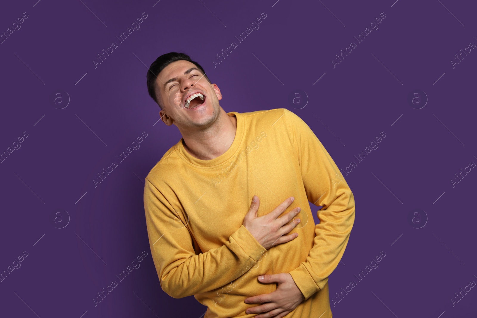 Photo of Handsome man laughing on purple background. Funny joke