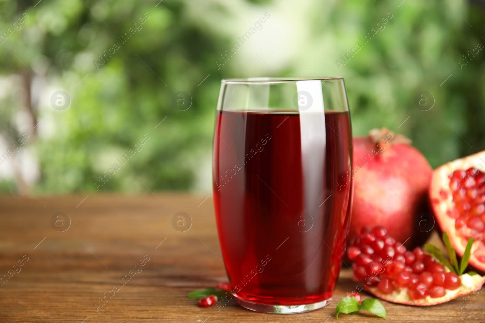 Photo of Pomegranate juice in glass and fresh fruits on wooden table outdoors, space for text