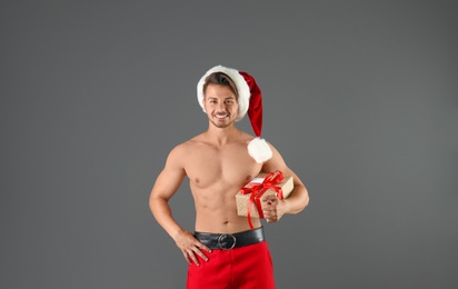 Photo of Shirtless sexy young Santa Claus with gift on color background