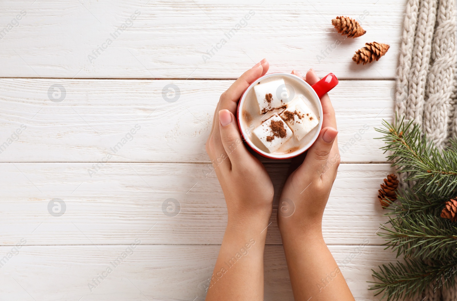 Photo of Woman holding cup of tasty cocoa with marshmallows on white wooden table, top view. Space for text