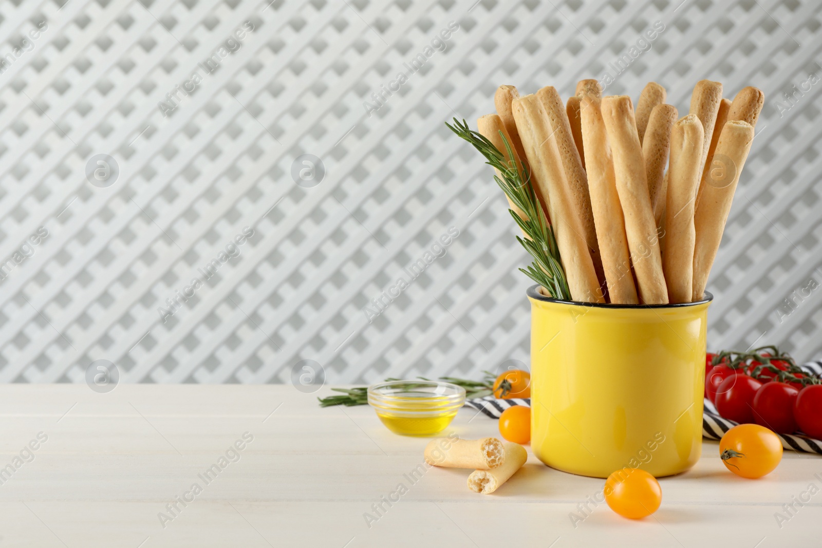 Photo of Delicious grissini sticks, rosemary and tomatoes on white wooden table. Space for text
