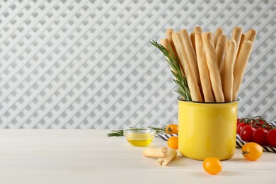 Delicious grissini sticks, rosemary and tomatoes on white wooden table. Space for text