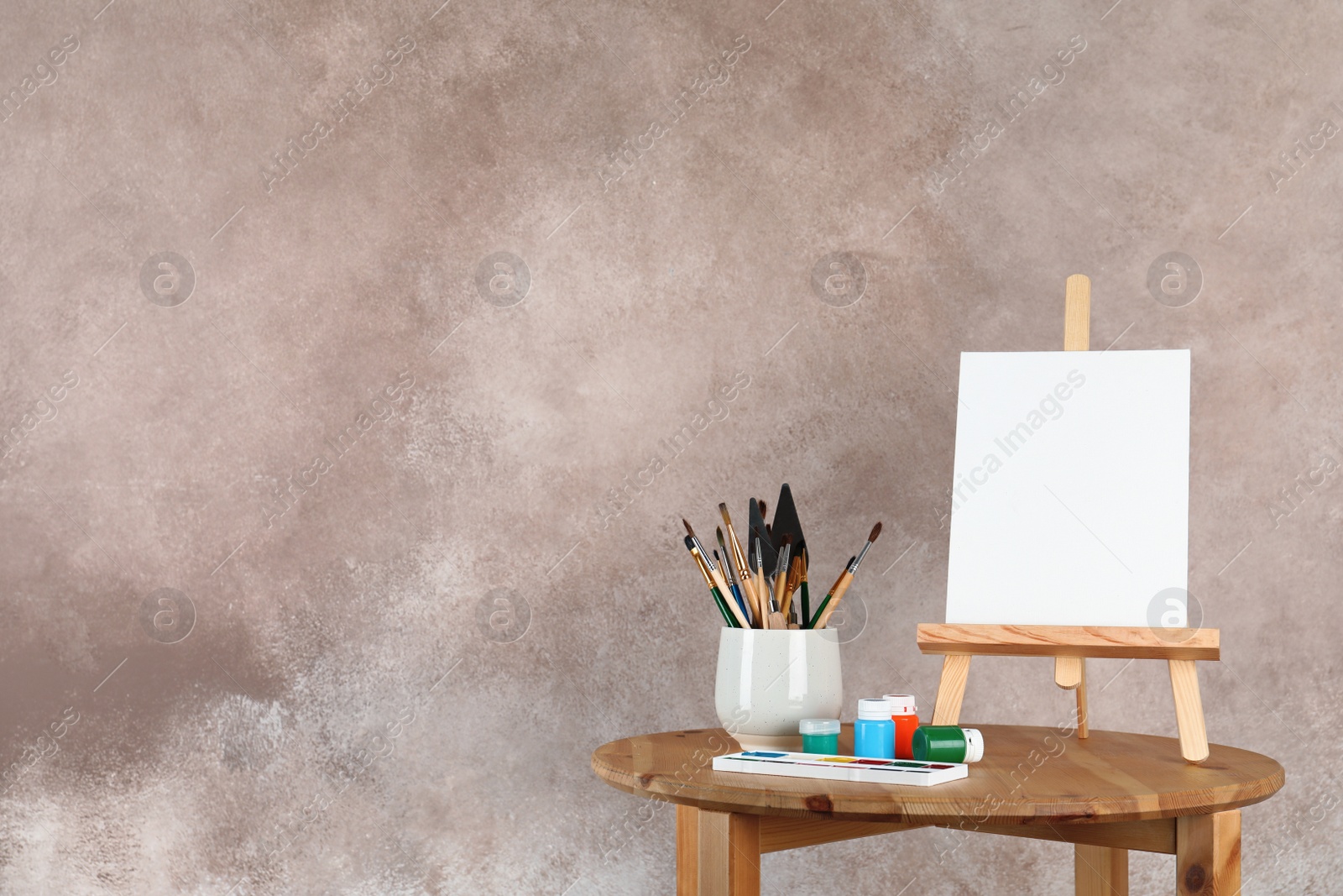 Photo of Wooden easel with blank canvas board and painting tools for children on table near color wall. Space for text