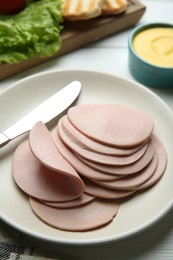 Slices of delicious boiled sausage and knife on white wooden table