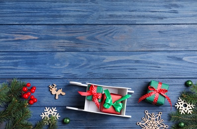 Flat lay composition with sleigh, fir tree branches and gift boxes on blue wooden table, space for text