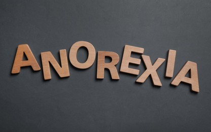 Word Anorexia made of wooden letters on dark grey background, flat lay